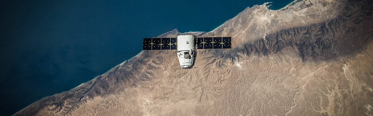 Imagen desde arriba en la que se ve un satélite sobrevolando parte de tierra y parte de mar